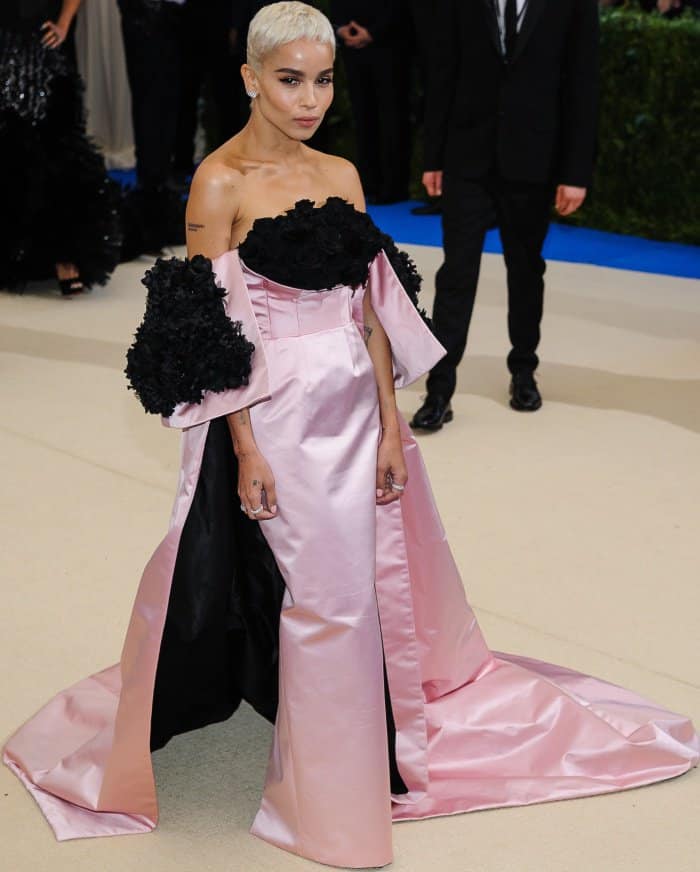 Zoë Kravitz showcases the architectural beauty of her custom Oscar de la Renta gown featuring pale-pink duchesse satin, sculpted black floral appliqués, and a sweeping cape-backed column silhouette.