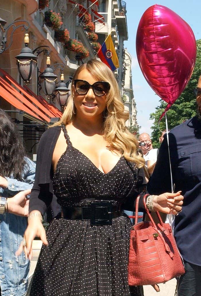 Mariah smiled as she carried a metallic heart-shaped balloon gifted by fans, adding a playful touch to an otherwise understated palette of black, nude, and rich burgundy tones