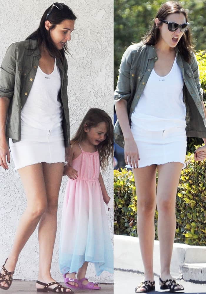 Gal Gadot keeps it effortlessly stylish in a white mini skirt, a casual 'Peace' tank, and an army green jacket, paired with studded sandals for a chic yet relaxed daytime look