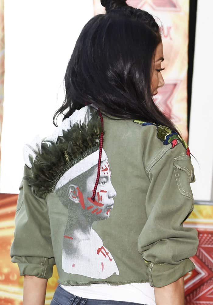 From the back, the cropped military jacket’s feathered graphic adds edge, contrasting with the sleek, feminine lines created by the heels below