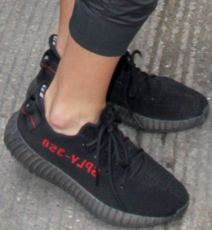 Khloé Kardashian wears Adidas Yeezy Boost 350 V2 "Core Black Red" sneakers featuring black Primeknit uppers, full-length Boost midsoles, and the signature red "SPLY-350" side stripe