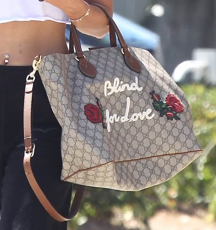 Brown leather trim, floral embroidery, and "Blind for Love" lettering add dimension to the Gucci tote's GG Supreme monogram canvas