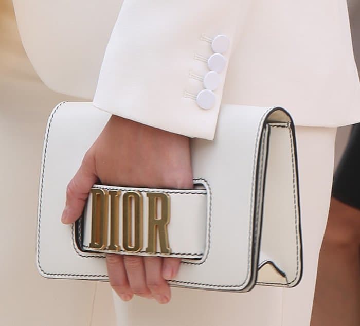 Gemma Arterton carries a structured white Dior flap clutch featuring bold gold logo hardware and contrast stitching—perfectly complementing her sleek suit