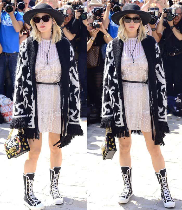 Jennifer Lawrence puts a playful twist on Parisian street style with a sheer lace dress, oversized fringe cardigan, lace-up Dior sneakers, and a bold embroidered J’Adior bag