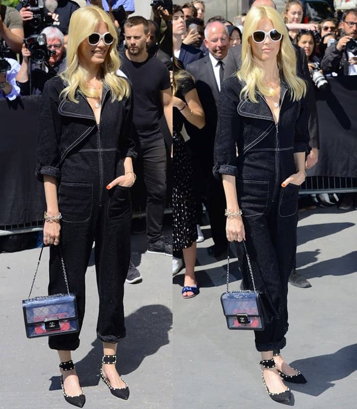 Claudia Schiffer keeps it cool in a black Chanel jumpsuit with contrast stitching, pairing it with studded flats, oversized sunglasses, and a transparent Chanel flap bag