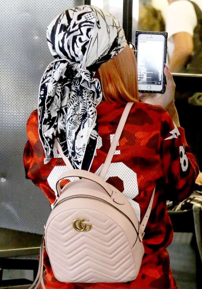 From behind, Blac Chyna is seen recording on her phone, while showing off a light pink, quilted Gucci backpack with a prominent GG logo