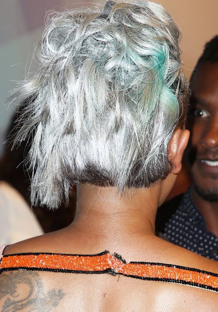 From the back, the singer’s cropped silver hairstyle and torn dress strap are visible, revealing the physical aftermath of the tense exchange while her styling remains otherwise intact