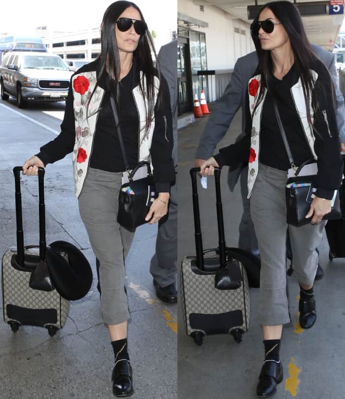 Demi Moore arriving at LAX in a floral-embroidered bomber jacket, grey pants, and black leather slip-on shoes