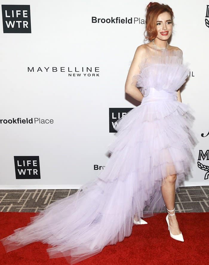 From a three-quarter angle, the cascading tulle skirt reveals the gown’s sculptural volume and soft movement as she smiles for photographers