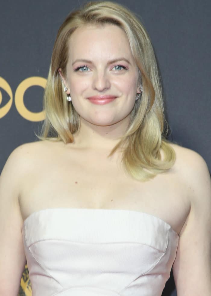 Elisabeth Moss wears her blonde hair in soft, side-parted waves and accessorizes with elegant drop earrings featuring sparkling stones