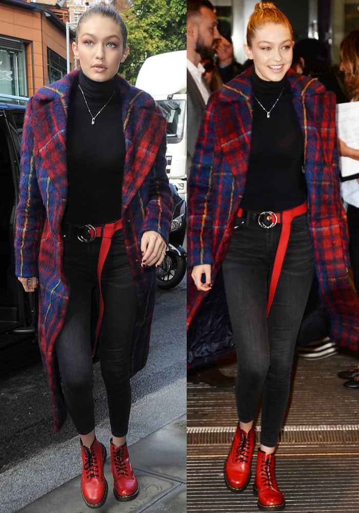 Gigi Hadid's ensemble features a striking plaid coat, designed with a vibrant red and blue multi-check pattern and a long, structured silhouette, paired with sleek black stretch denim jeans for a balanced look