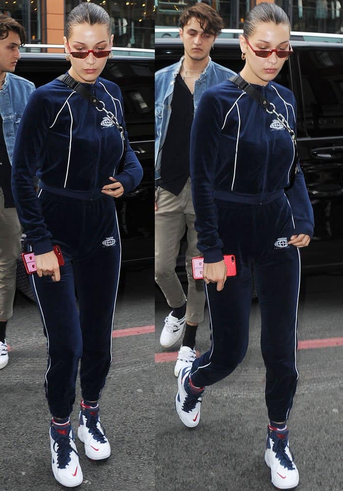 Bella Hadid's sporty ensemble features a deep navy velvet tracksuit, designed with a sleek zippered jacket and matching slim-fit track pants, accented by contrasting white piping for a modern, athletic aesthetic