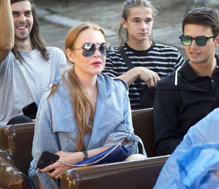 Lindsay Lohan stays stylish in aviators and a denim wrap dress as she gets ready for a theme park ride with friends in Madrid