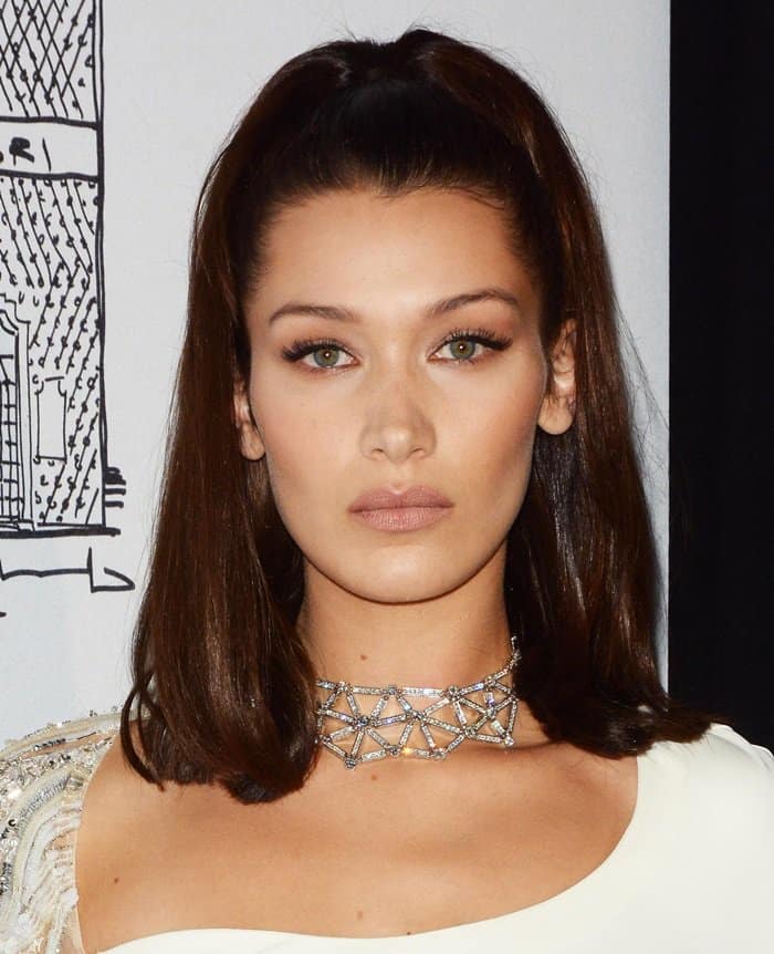Bella Hadid keeps her glam sleek and modern with a half-up hairstyle, bronzed makeup, and an intricate diamond Bulgari choker that perfectly complements her white Roberto Cavalli evening look
