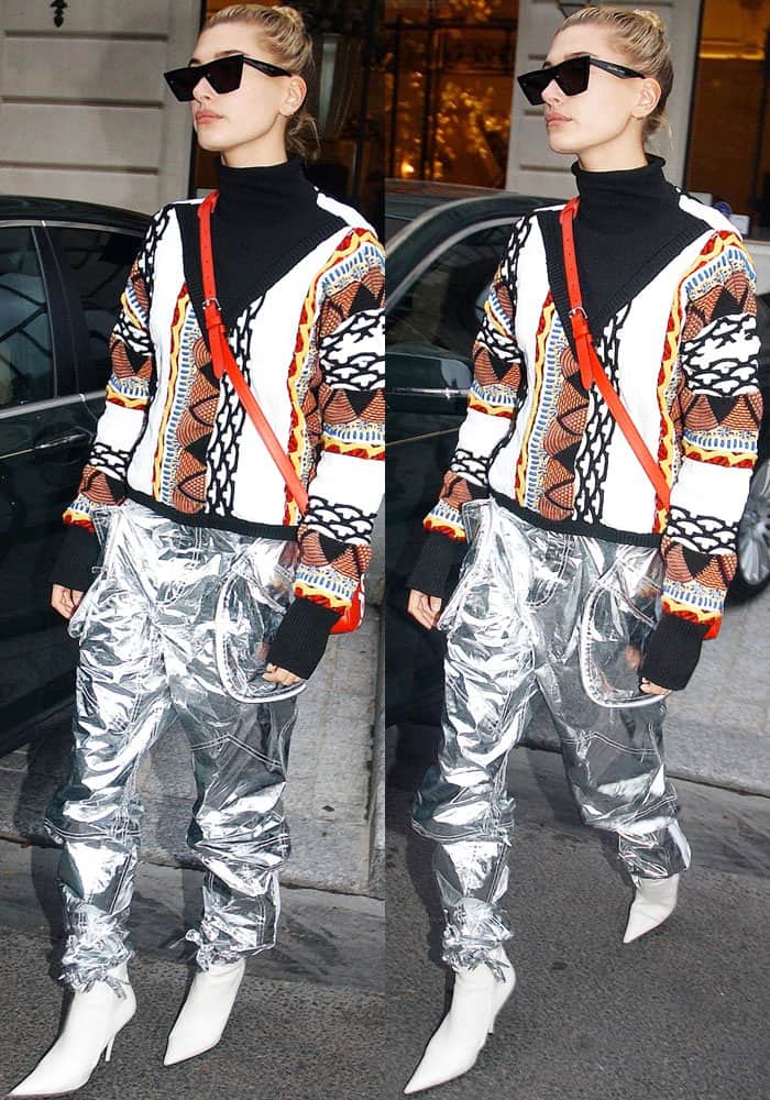 Hailey Bieber steps out in Paris wearing futuristic silver metallic pants, a colorful Aalto roll-neck sweater, and sharp white Balenciaga “Knife” boots—blending streetwear boldness with high-fashion edge