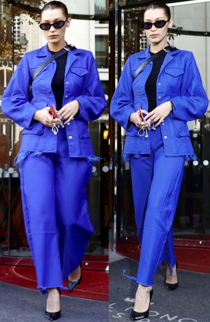 Bella Hadid, with her hair slicked back into a sleek style, carrying her phone and keys and wearing a vibrant blue ensemble with black pointed-toe pumps