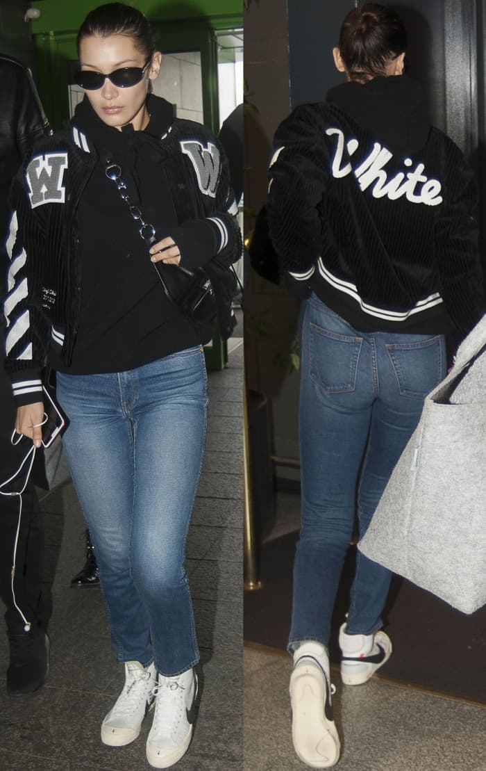 Bella Hadid arrives at Milan Airport on September 24, 2017, wearing an Off-White varsity jacket, Alexander Wang Attica fanny pack, Nike x Off-White Blazer Mid sneakers, and Roberi Fraud Betty sunglasses for a sporty, street-style look