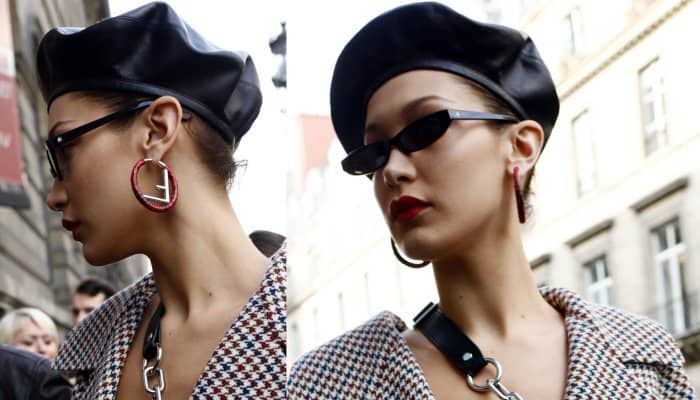 Bella Hadid pairs a black leather beret with bold hoop earrings and striking red lipstick, complemented by sleek cat-eye sunglasses for a chic, Parisian-inspired look