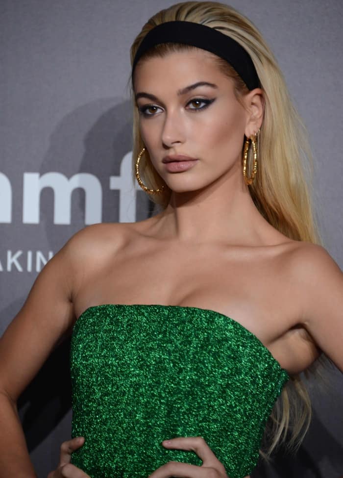 Hailey Baldwin channels retro glam with a sleek headband, bold hoop earrings, and dramatic winged eyeliner, perfectly complementing her strapless green gown