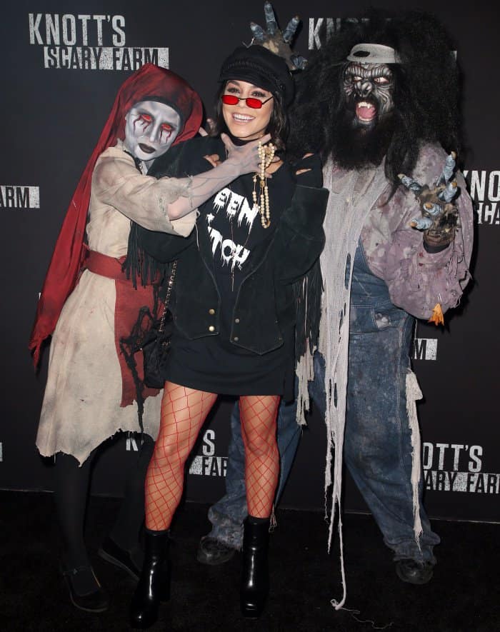 Vanessa Hudgens embraces the Halloween spirit by posing between costumed performers, balancing playful theatrics with a grounded, all-black platform boot silhouette