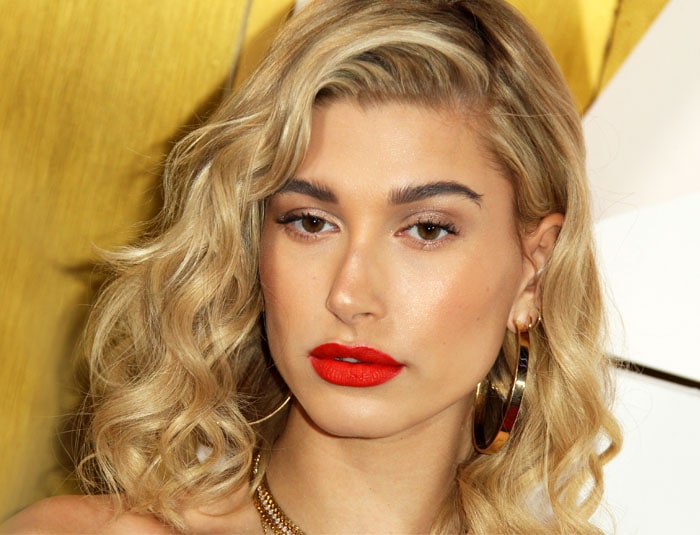 Hailey Baldwin stuns with voluminous blonde curls, bold red lips, and radiant makeup at the #REVOLVE Awards