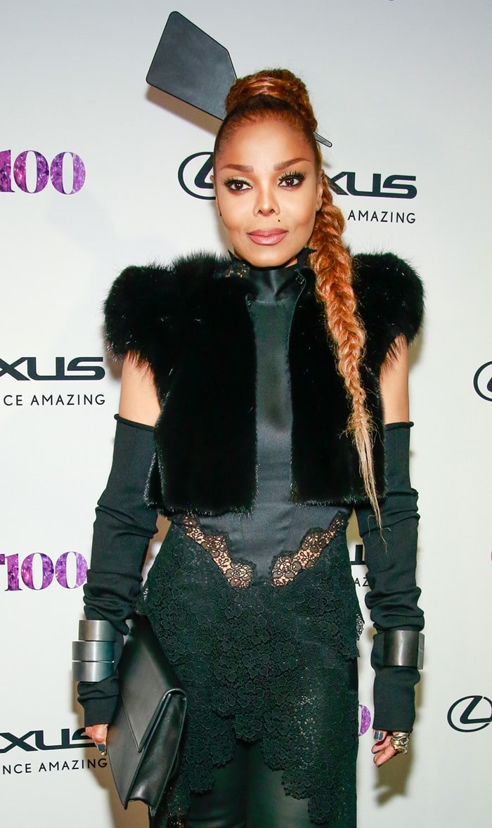 Janet Jackson accessorized her edgy ensemble with bold silver cuff bracelets, fingerless gloves, a sleek rectangular clutch, and a unique paddle-shaped hair accessory
