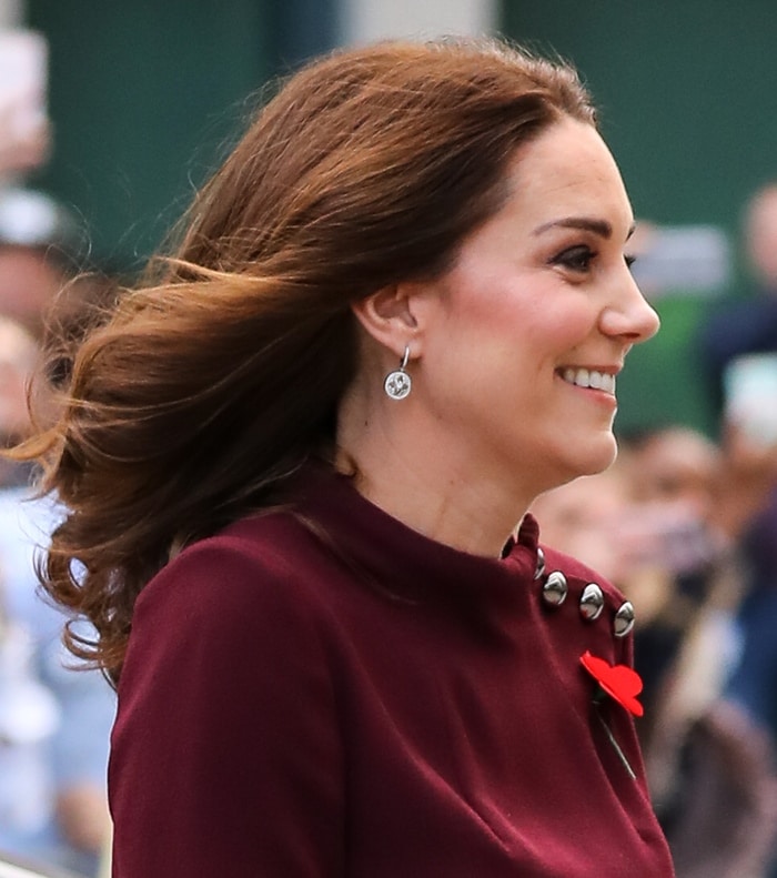 Kate Middleton radiates elegance, accessorizing her wine-colored tunic dress with Mappin Webb 'Empress' diamond drop earrings and a striking red Remembrance poppy pin