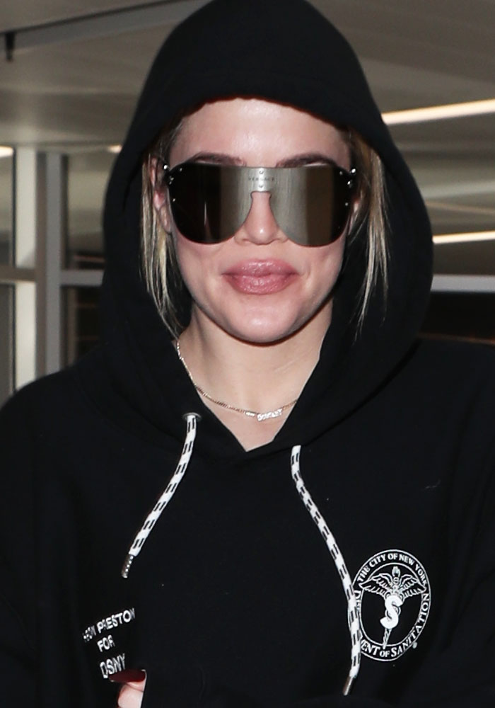 Khloé Kardashian epitomizes airport-chic in oversized Versace sunglasses and a Heron Preston hoodie, showcasing a blend of comfort and high-fashion accessories for travel