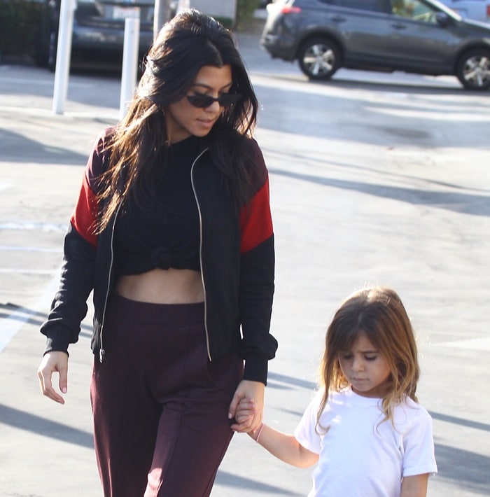 Kourtney Kardashian holds hands with daughter Penelope Disick while showing off her toned abs in a knotted black tee and maroon trousers