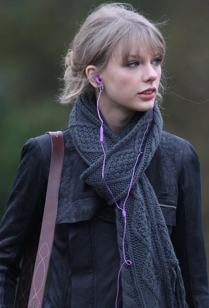 Taylor Swift embraces effortless elegance with a soft, tousled updo and wispy bangs, pairing her fresh-faced makeup and subtle pink lip with a chunky gray knit scarf