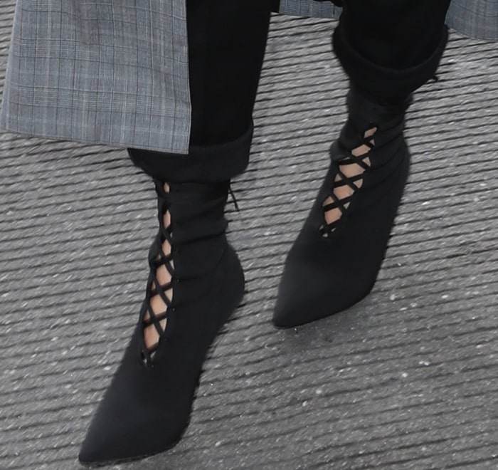 Chrissy Teigen steps out in sleek black Yeezy Season 5 lace-up sock boots, featuring a pointed toe and crisscross front lacing that sharpens her off-duty airport look