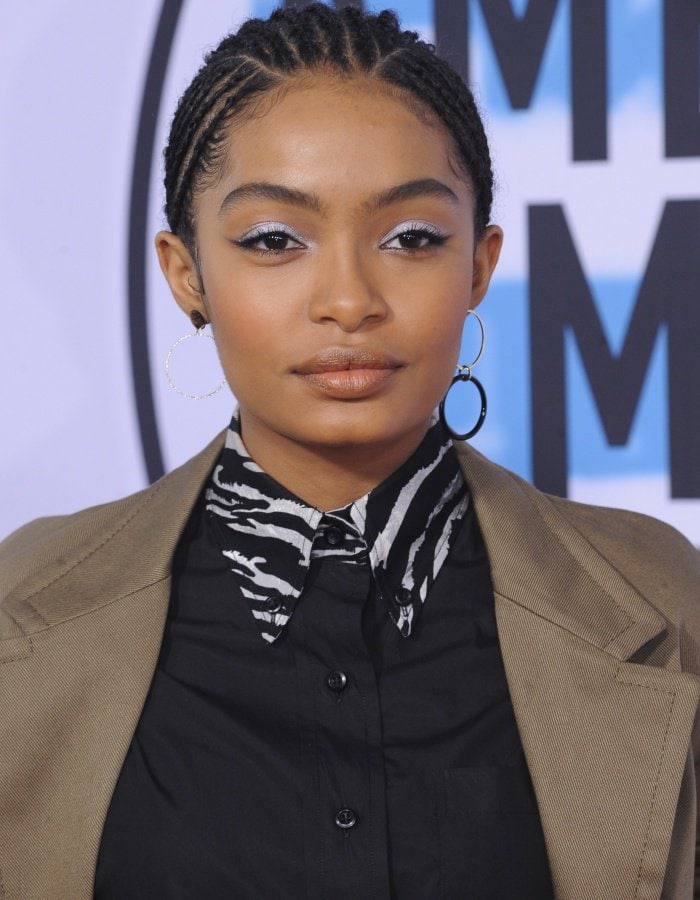 Yara Shahidi enhances her look with shimmering silver eye makeup that adds a touch of glamour, a sleek braided hairstyle for a modern edge, and bold Mateo jewelry to complete the chic ensemble