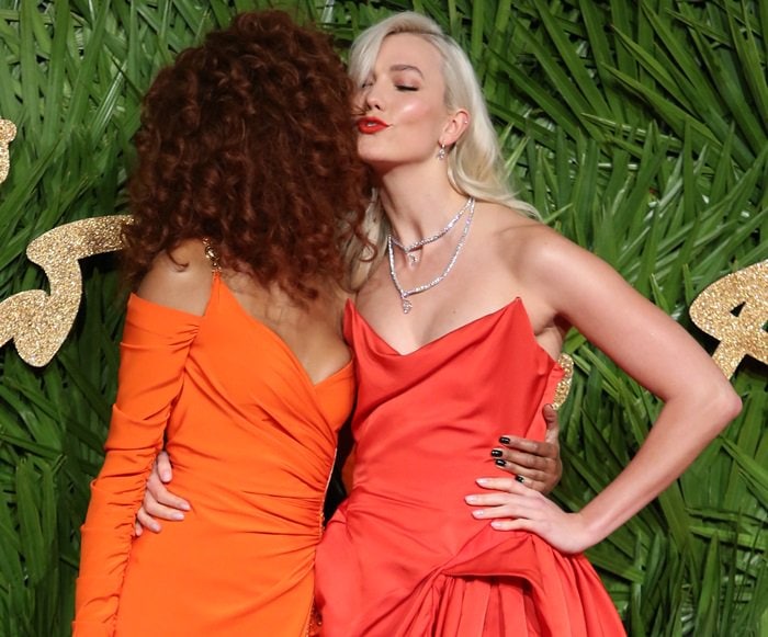 The rich red satin contrasts vividly against the green backdrop, underscoring the look’s timeless red-carpet impact