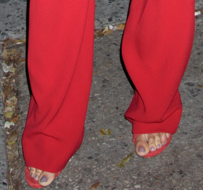 Close-up of Joan Smalls wearing minimalist red Stuart Weitzman sandals beneath wide-leg red trousers
