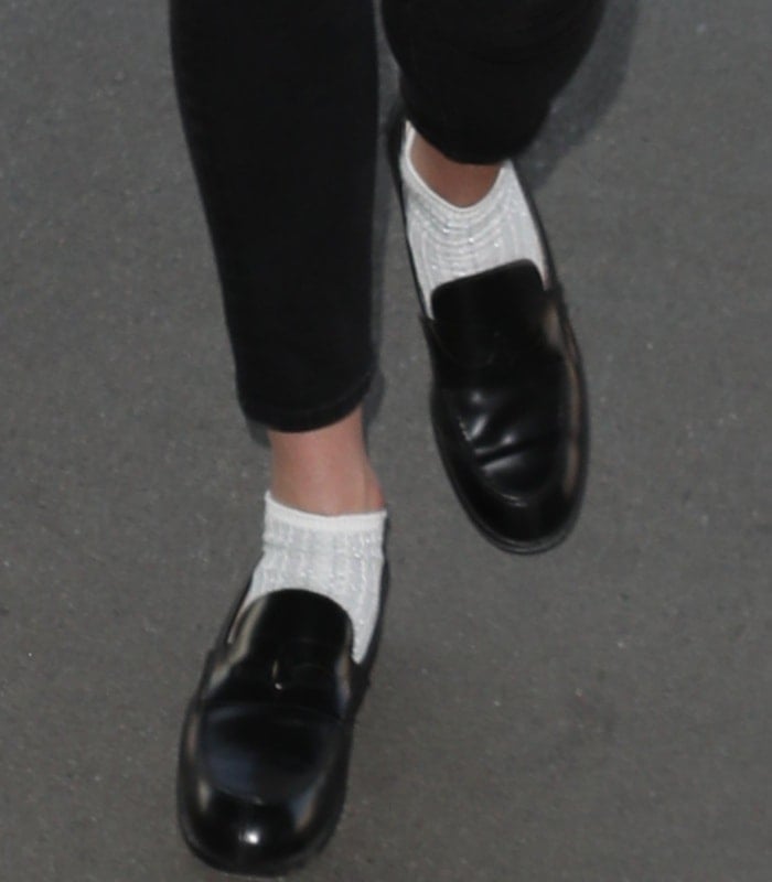 Karlie Kloss grounds her airport look with glossy black Christian Louboutin Montezumo Donna loafers, styled with ribbed white socks for a modern, menswear-inspired take on polished travel dressing