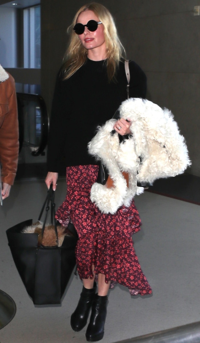 Kate Bosworth perfects airport style with a black sweater, floral ruffled skirt, and chic ankle boots, adding a cozy shearling jacket for extra warmth