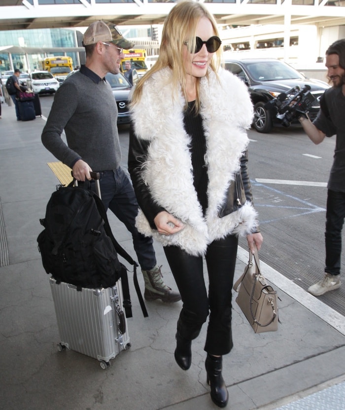 Kate Bosworth embraces edgy airport style with a statement shearling-lined leather jacket, sleek black pants, and chic ankle boots, accessorized with a structured handbag and oversized sunglasses
