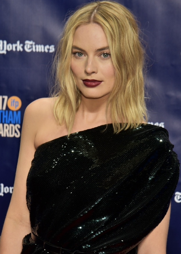 Margot Robbie elevates her look with tousled waves and a bold dark red lip, balancing edgy elegance with timeless beauty