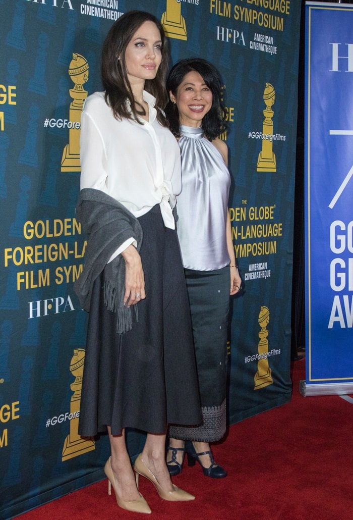 Angelina Jolie posed with author and activist Loung Ung at the HFPA and American Cinematheque’s Golden Globe Foreign Language Nominees Series Symposium, wearing nude pointy-toe pumps with a flowing navy midi skirt and an oversized white oxford shirt