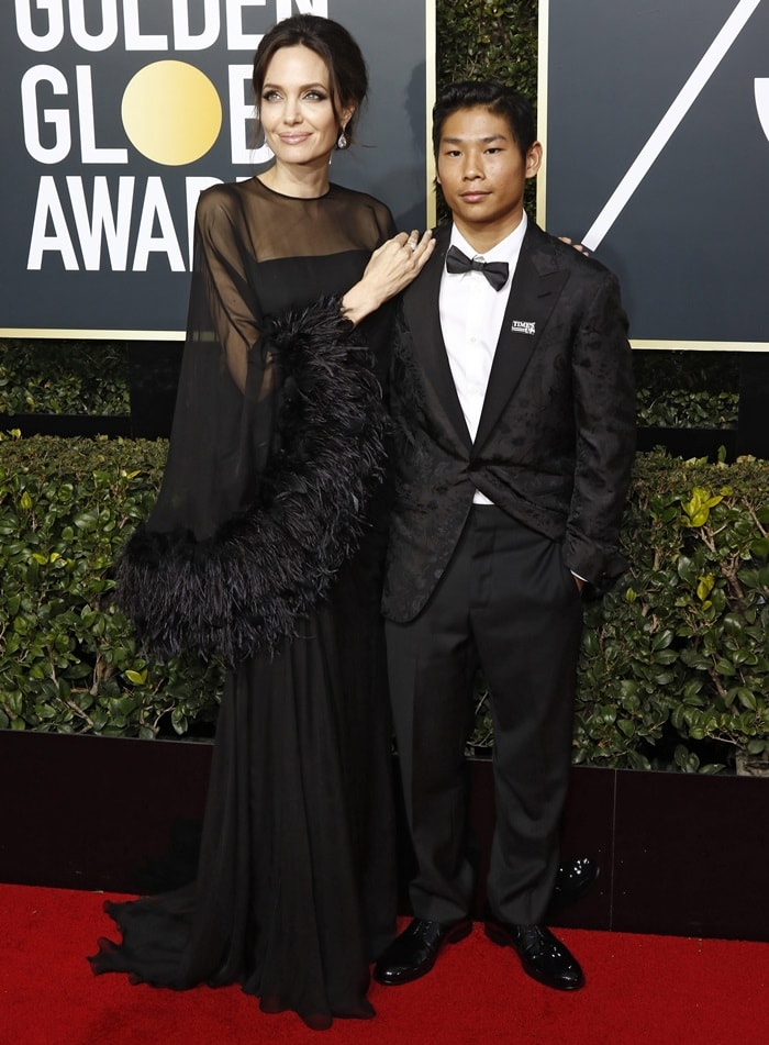 Angelina Jolie and Pax Jolie-Pitt coordinated in monochromatic eveningwear on the Golden Globes red carpet, with Jolie’s flowing chiffon Versace gown contrasting against Pax’s textured black tuxedo jacket