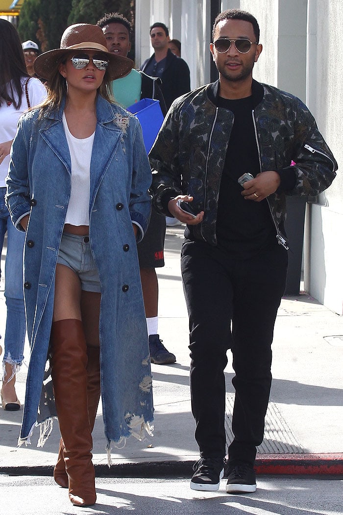 Chrissy Teigen and John Legend step out for a lunch date in Beverly Hills — she in Saint Laurent thigh-high boots and a distressed Alexander Wang denim trench, while he keeps it sleek in a camouflage bomber jacket and black sneakers