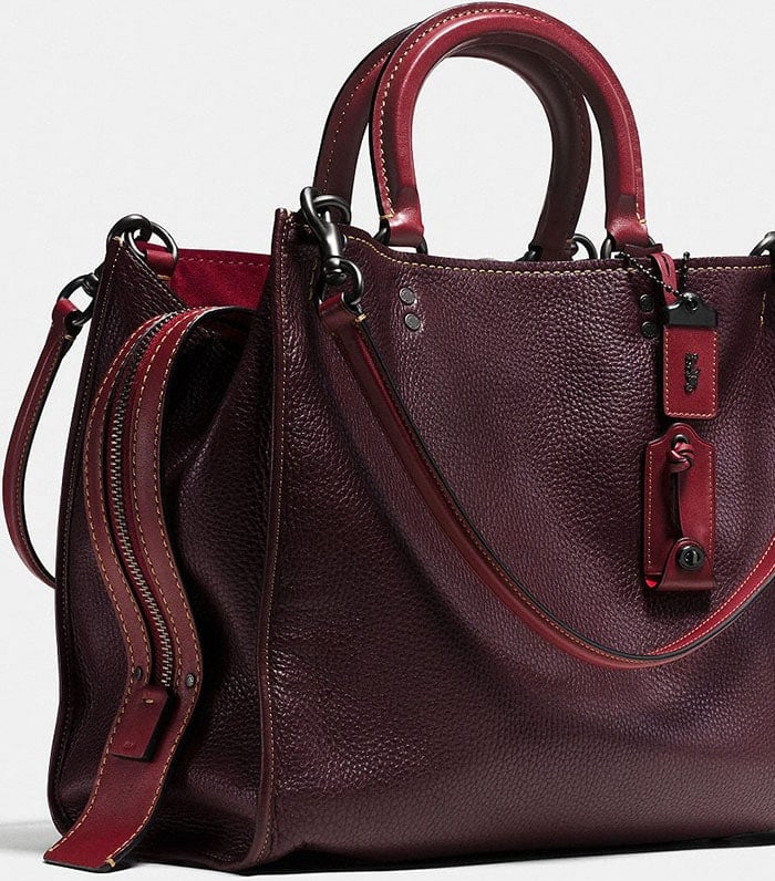 This structured burgundy Coach satchel showcases dual top handles, contrast stitching, and rich leather texture, highlighting the brand’s expert attention to materials and finish