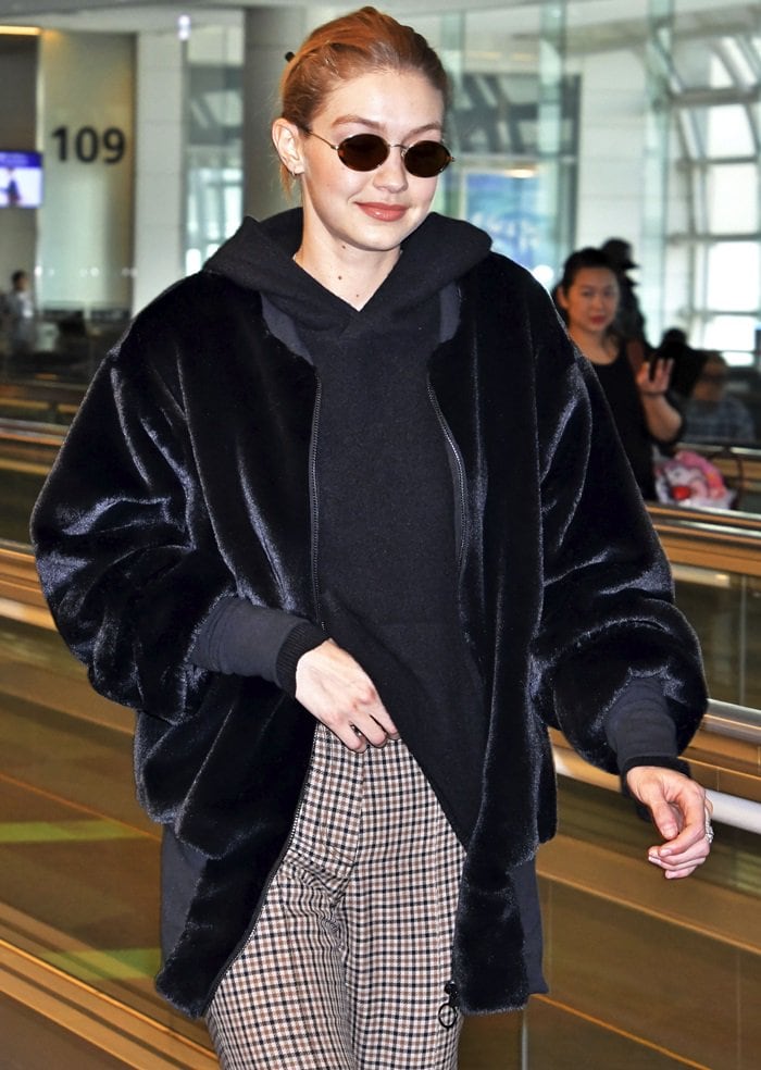 Gigi Hadid walks through the airport in a plush black velvet bomber jacket paired with a hoodie and checkered pants