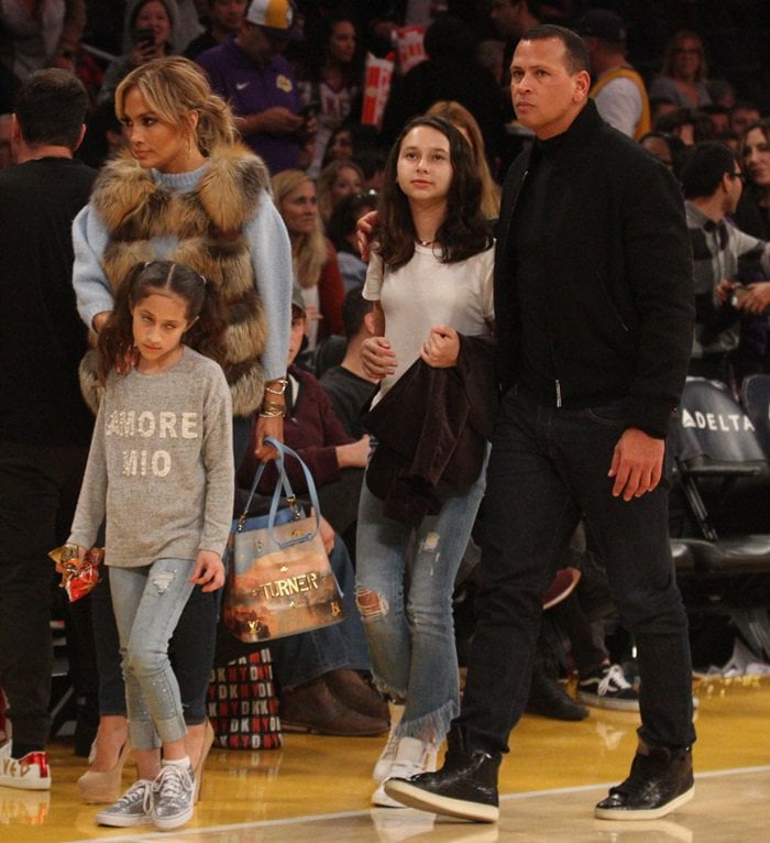 Jennifer Lopez elevates her courtside style in a sky blue Tibi alpaca sweater, two-tone fur vest, Louis Vuitton x Jeff Koons Turner NeoNoe bag, Hermes cuff, and leg-elongating Giuseppe Zanotti double platform pumps in crème