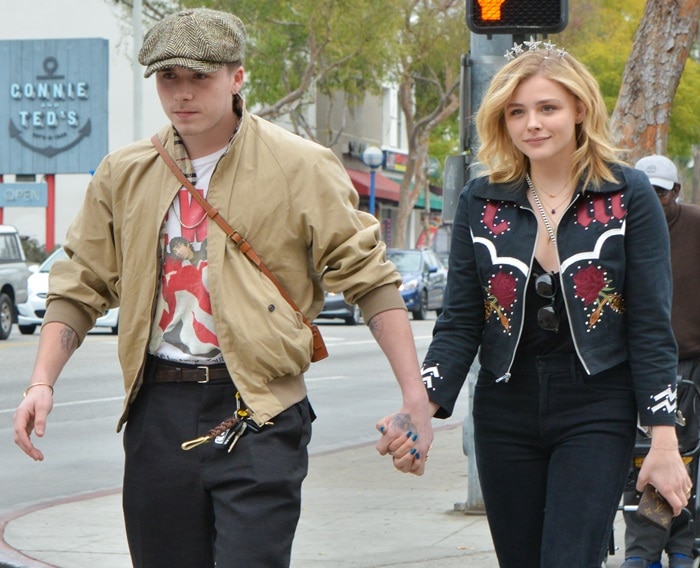 Chloë Grace Moretz keeps it stylish in a black embroidered jacket, black jeans, and a star tiara, while Brooklyn Beckham pairs a vintage bomber jacket with a graphic tee and a baker boy hat