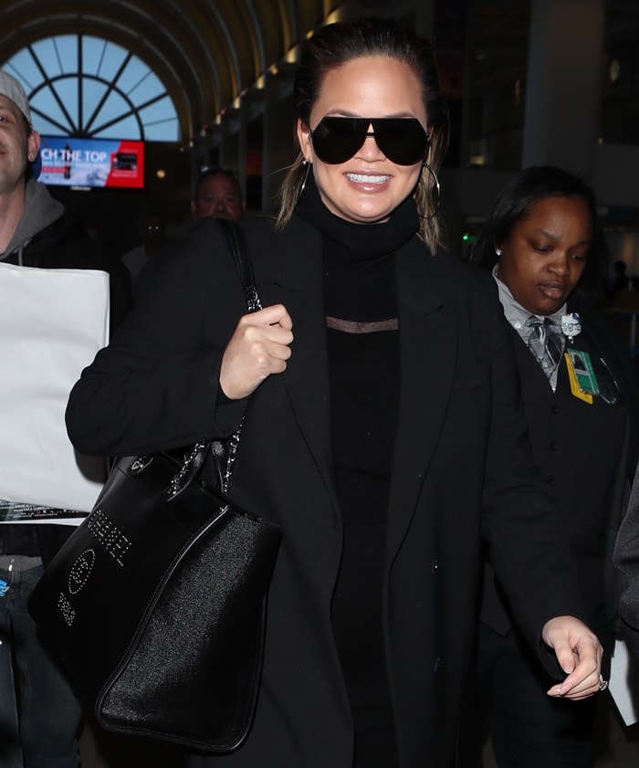 Chrissy Teigen wearing a chic mini dress and a black coat at Los Angeles International (LAX) on February 23, 2018