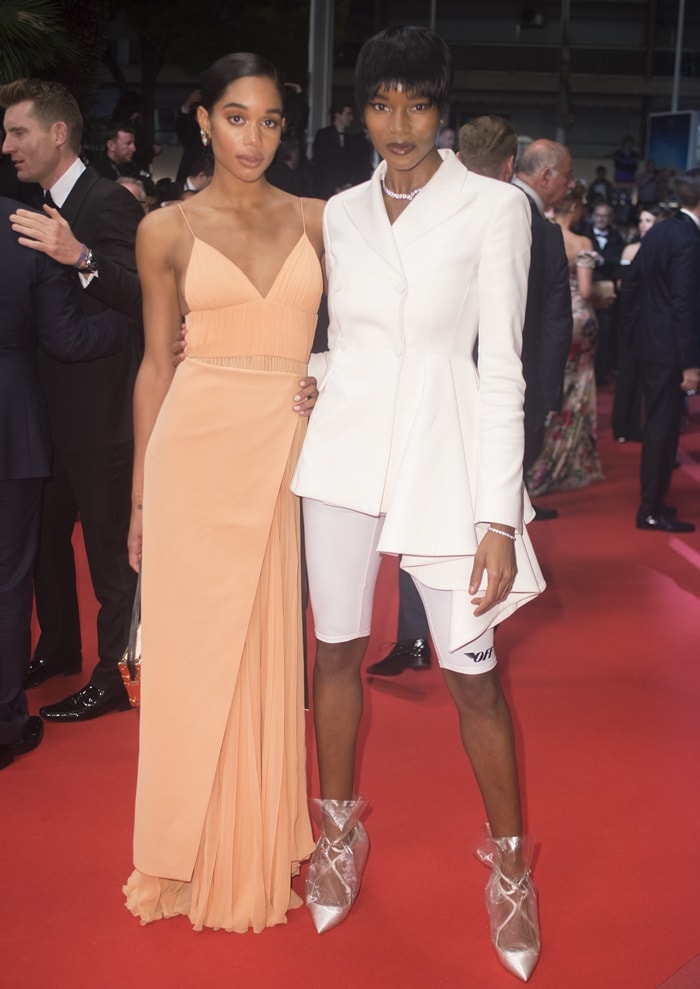 Laura Harrier stuns in an elegant peach gown alongside Damaris Lewis, who makes a bold statement in a white blazer, cycling shorts, and Off-White x Jimmy Choo PVC-wrapped boots, on the red carpet at the premiere of BlacKkKlansman during the 2018 Cannes Film Festival on May 14, 2018