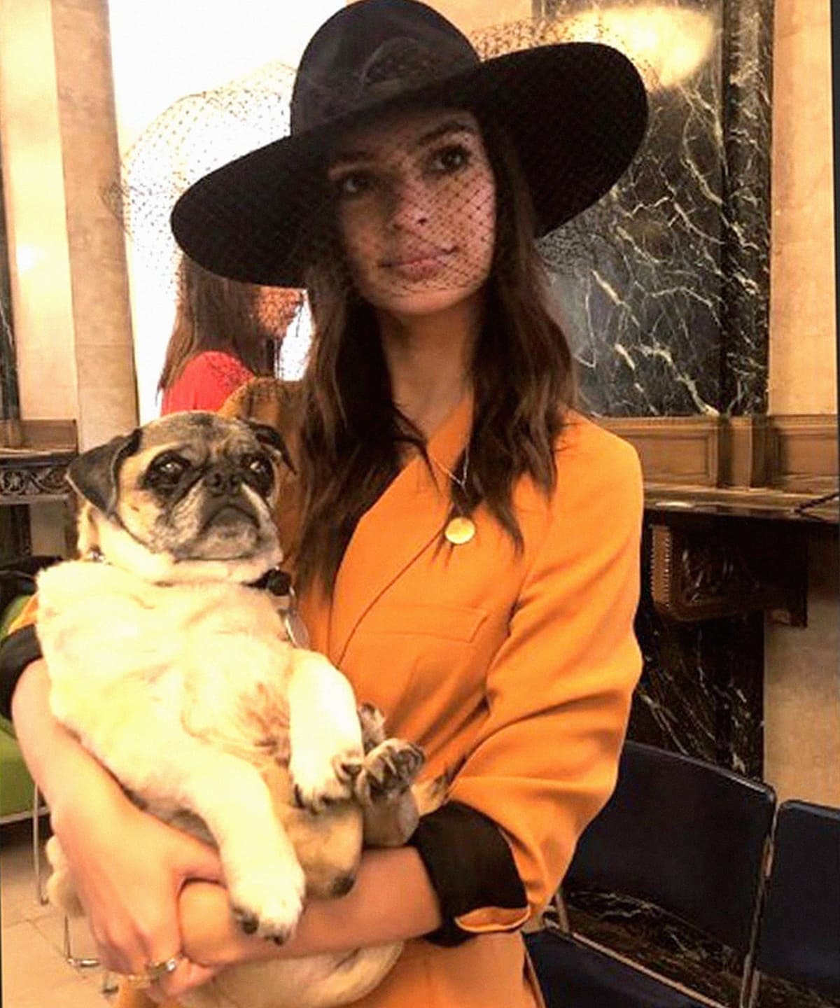 Emily Ratajkowski holding her dog while wearing a mustard-yellow Zara suit and a black netted fedora at her New York City Hall wedding