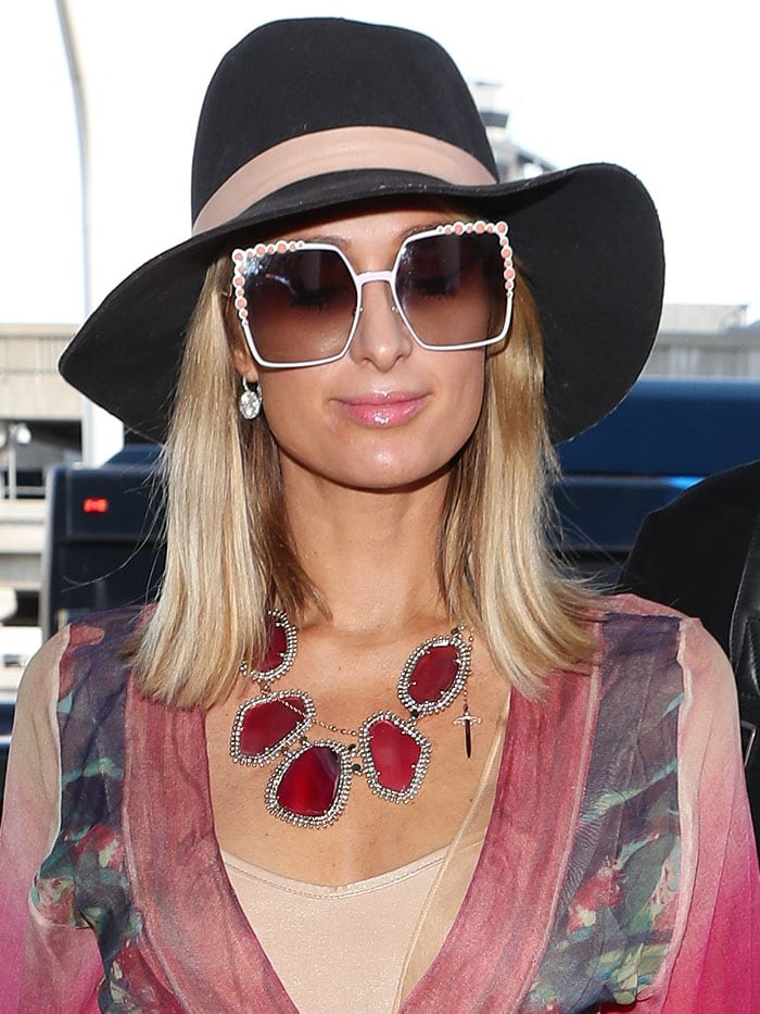 Paris Hilton over-accessorized with a black, wide-brimmed hat, Fendi "White Can Eye" embellished sunglasses, and a massive Kendra Scott "Ava" pink agate necklace