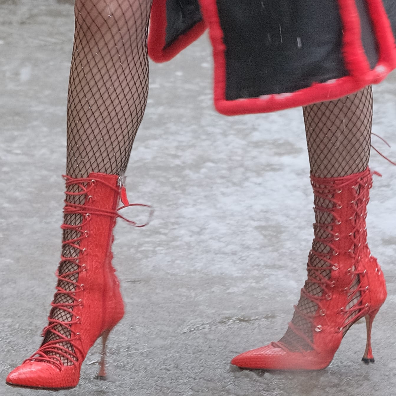 Bella Thorne steps out in striking red snakeskin “Drury Lane” lace-up boots by Liudmila, the Victorian-inspired silhouette featuring corset-style lacing and sharp stiletto heels that add dramatic contrast to her fishnet tights